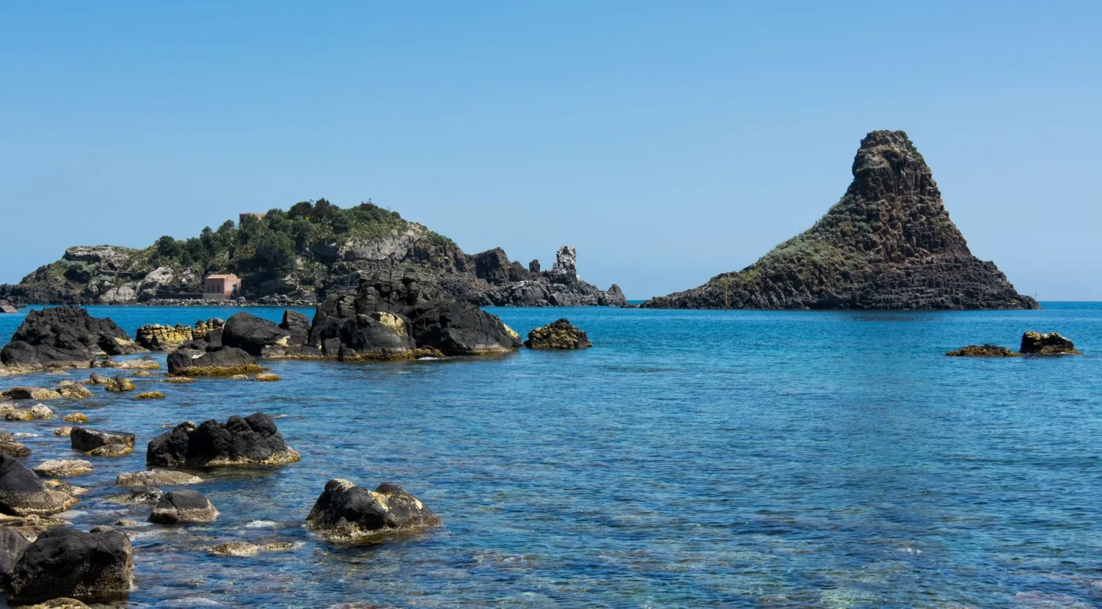 The Faraglioni dei Ciclopi sea stacks rising from the turquoise water off Aci Trezza, with Isola Lachea behind