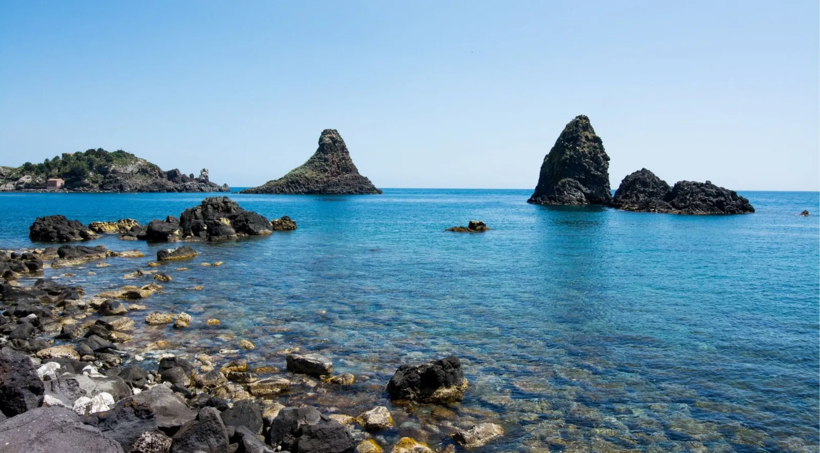 Basalt sea stacks of the Cyclops Islands seen from the rocky shoreline near Aci Trezza