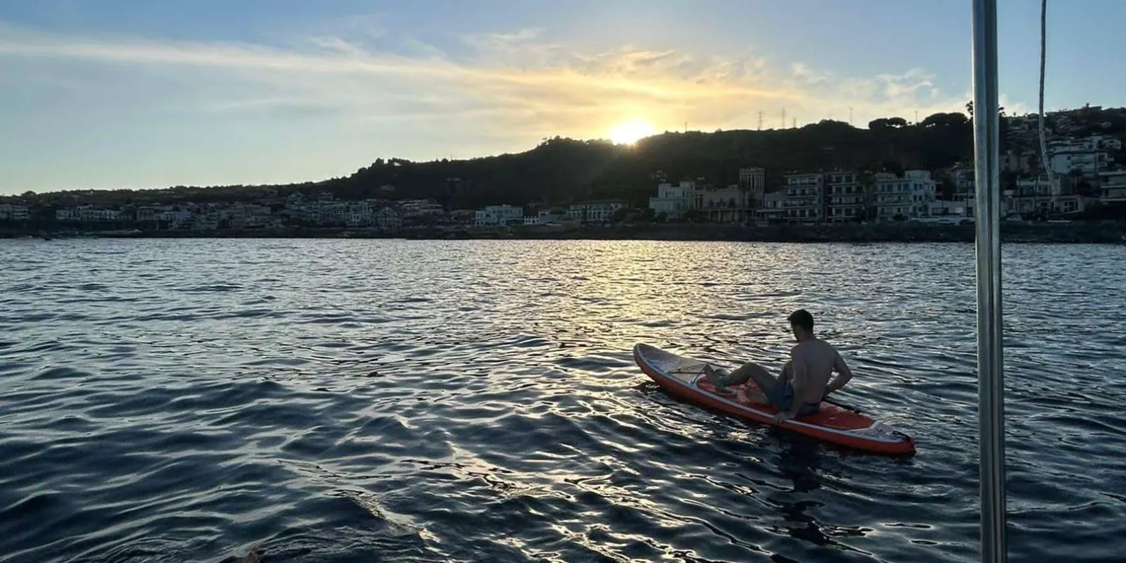 Guest paddleboarding at sunset near Aci Trezza with the coastal town glowing in the evening light